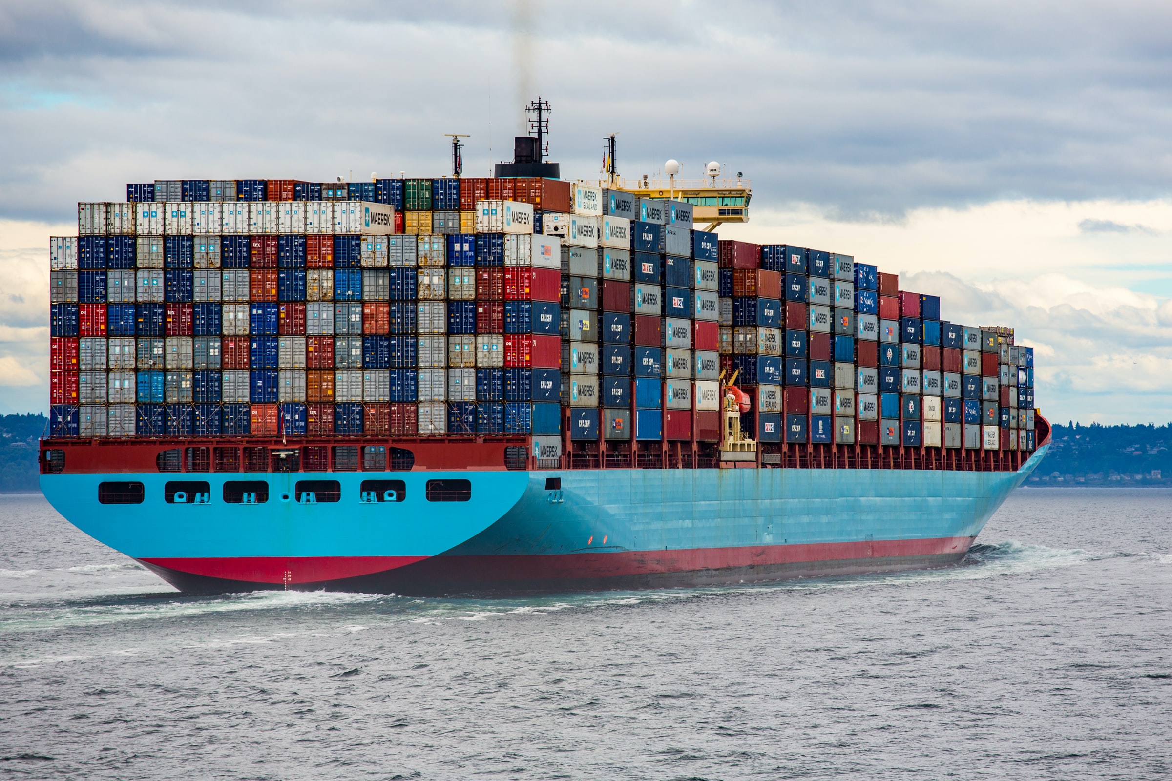 A blue container ship on the water, stacked with containers.